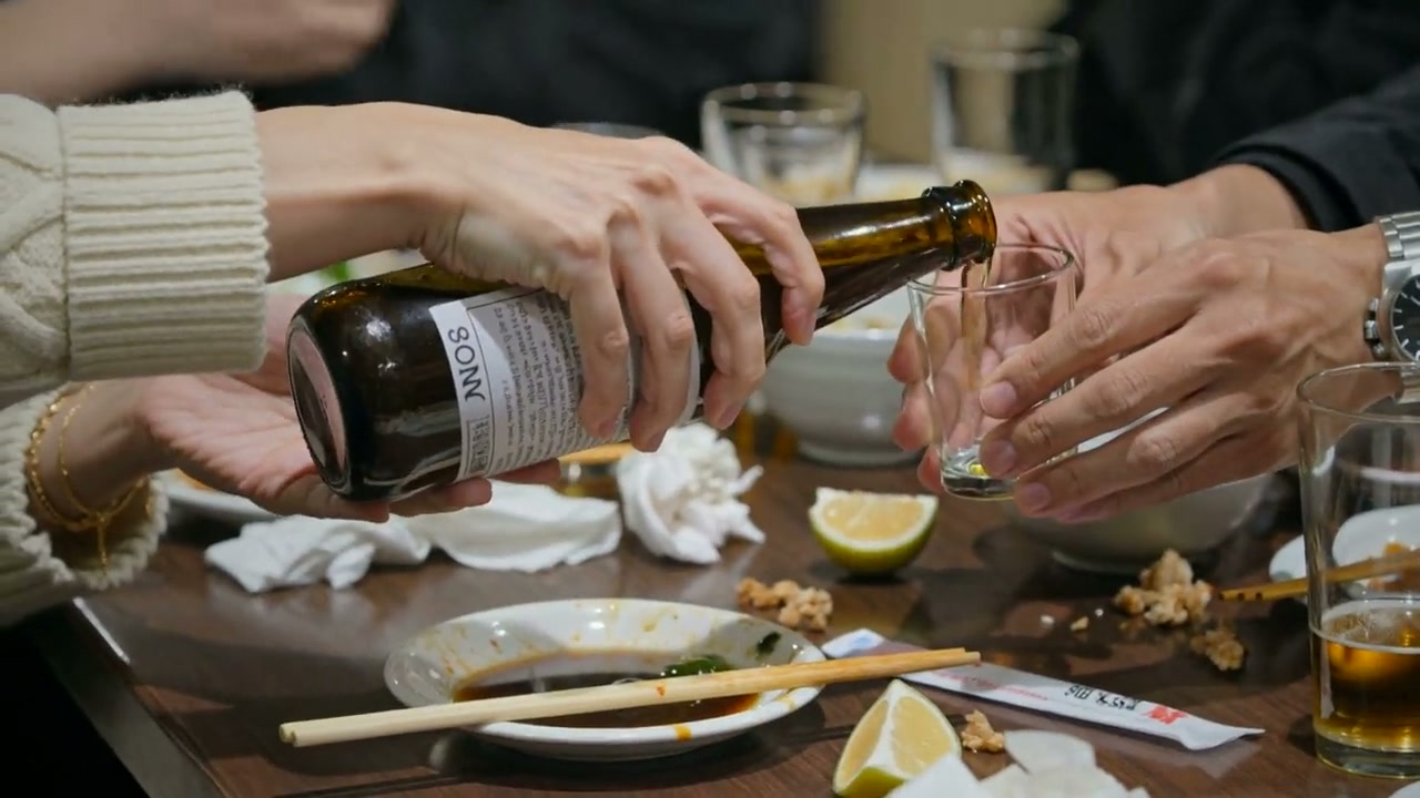 瓶ビールをグラスに注いでいる手元。卓には取り皿やおしぼりが並んでいる